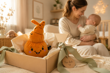 Lenabo-Kuscheltier Mia die Muschel als liebevolles Geschenk zur Geburt in einer hochwertig gestalteten Geschenkbox mit Mutter und Baby im Hintergrund.