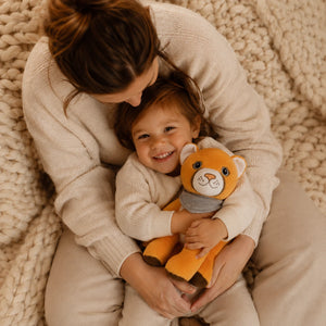 Kind sitzt lachend im Schoß seiner Mutter auf einer hellen Kuscheldecke und kuschelt mit Lenabie Tali die Puma-Dame. Die warme Familienatmosphäre und das Audio-Kuscheltier für Kinder stehen für gemeinsame Zeit mit Hörspielen, Musik und altersgerechten Geschichten.