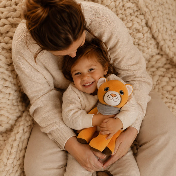Kind sitzt lachend im Schoß seiner Mutter auf einer hellen Kuscheldecke und kuschelt mit Lenabie Tali die Puma-Dame. Die warme Familienatmosphäre und das Audio-Kuscheltier für Kinder stehen für gemeinsame Zeit mit Hörspielen, Musik und altersgerechten Geschichten.