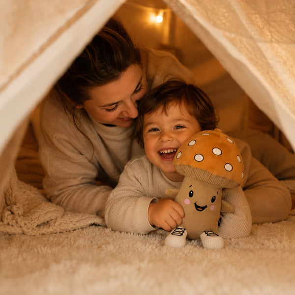 Kind und Mutter kuscheln gemeinsam in einem Spielzelt mit Lenabie Felix dem Pilz. Das interaktive Audio-Kuscheltier für Kinder begleitet die gemeinsame Hörspiel-, Vorlese- und Kuschelzeit und schafft eine warme, geborgene Atmosphäre im Kinderzimmer. Das Kind lächelt fröhlich und hält die freundliche Pilzfigur im Arm.