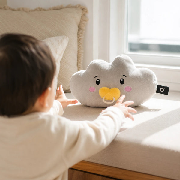 Kleinkind streckt neugierig die Arme nach Lenabie Lina der Wolke aus, die auf einer sonnigen Fensterbank sitzt. Das liebevoll gestaltete Audio-Kuscheltier für Kinder lädt zu Hörspielen, Musik und fantasievollen Geschichten in einer warmen und geborgenen Umgebung ein.